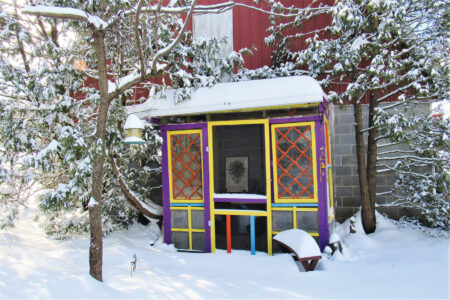 purple garden shed with yellow and red window trim in snowy yard